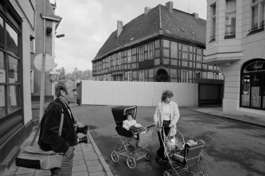 Christian Fenger mit zwei Kameras und Fototasche in der Eberswalder Altstadt, daneben eine Frau mit zwei Kinderwagen