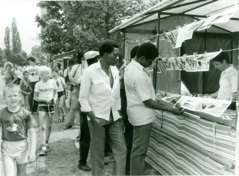 Zwei Männer aus Mosambik betrachten Fotografien an einem Stand, daneben Kinder und Besucher